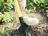 Tan boot pushing down on a yellow handled shovel going into the ground