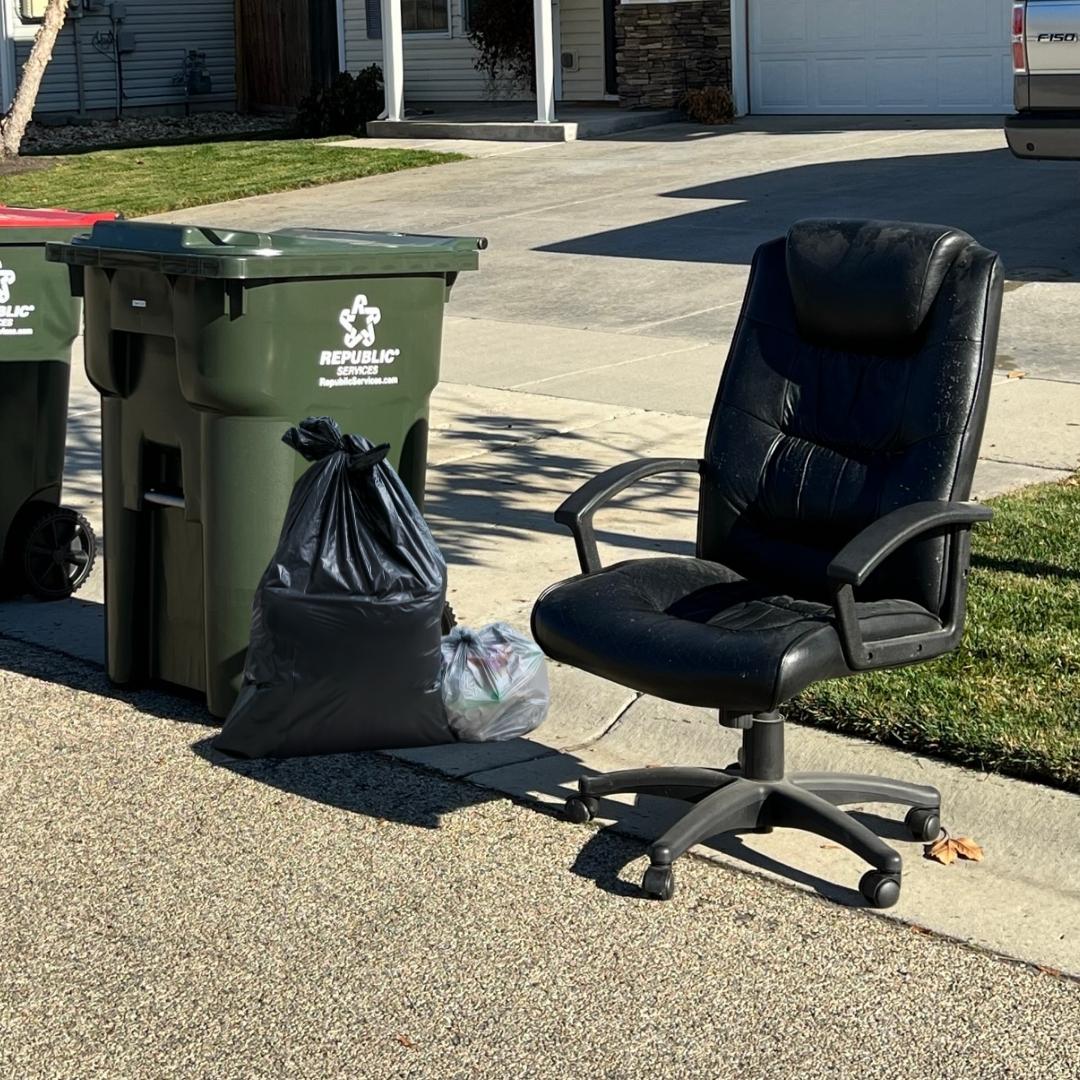 Bulky item, extra black trash bag, and a Republic Services green trash cart at the curb