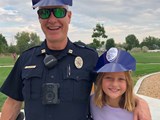 Police officer and a young girl posing with their police hats on at a park.