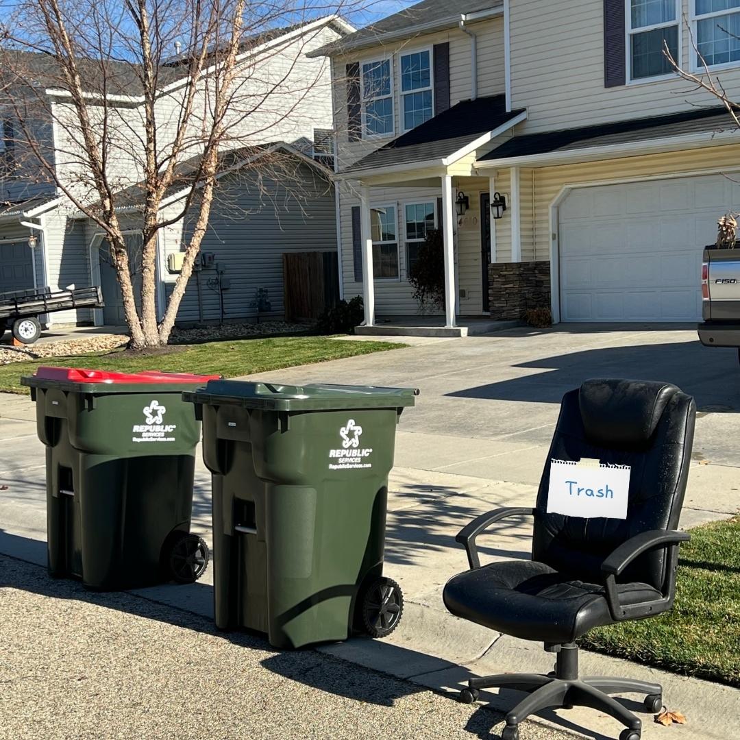 A trash cart, a recycling cart, and a bulky trash item (broken chair) on the curb.